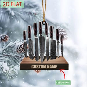 May include: A decorative ornament featuring a set of kitchen knives with dark wood handles and patterned blades. The knives are displayed on a wooden shelf with the text "CUSTOM NAME". The ornament is suspended by a gold string, with the text "2D FLAT" at the top.