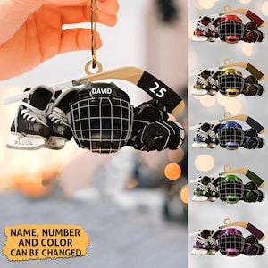 May include: A hockey-themed ornament featuring a black helmet with the name "DAVID", skates, gloves, and a hockey stick with the number "25". The text "NAME, NUMBER AND COLOR CAN BE CHANGED" is also visible. Several color variations are shown.