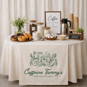 May include: A coffee station with a white tablecloth, featuring donuts, coffee beans, sugar, creamer, and a coffee maker. A sign reads "Coffee: The perfect blend." A runner displays "Caffeine Tammy's: More than just coffee."