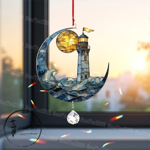 May include: A decorative lighthouse and moon ornament. The lighthouse is light blue with a yellow flag, set against a yellow moon and blue waves. A crystal prism hangs below, suspended by a red ribbon.