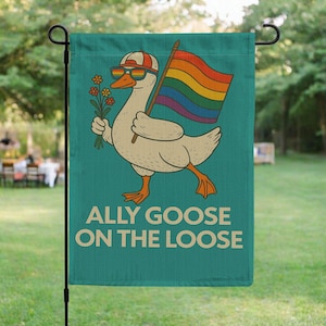 Puede incluir: Una bandera de jardín turquesa con un ganso de dibujos animados con gafas de sol y una gorra, sosteniendo una bandera arcoíris y flores. El texto "ALLY GOOSE ON THE LOOSE" está impreso debajo.