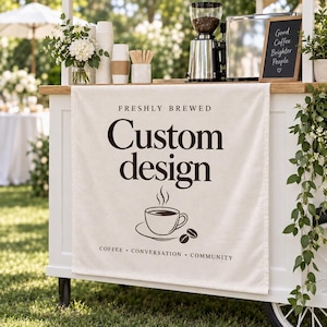 May include: A cream-colored fabric banner hanging on a white coffee cart. The banner features the text "FRESHLY BREWED", "Custom design", and "COFFEE • CONVERSATION • COMMUNITY" in dark brown, along with a graphic of a steaming coffee cup and beans.