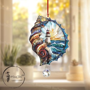 以下が含まれることがあります： 灯台と海のシーンが描かれたステンドグラスの貝殻のオーナメント。貝殻は青、緑、黄色で、下からクリスタルプリズムがぶら下がっています。