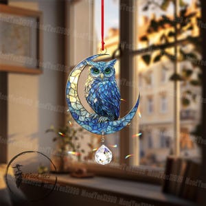 May include: A stained glass suncatcher featuring a blue owl perched on a crescent moon. The suncatcher has a crystal prism hanging from the bottom.
