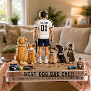 Puede incluir: Una pantalla acrílica transparente con un hombre con una camiseta "Dog Dad" con el número 01, rodeado de cinco perros. La base dice "Best Dog Dad Ever" con un mensaje de agradecimiento. Incluye un cuenco para perros, una pelota de tenis y un tarro de golosinas.