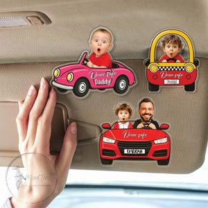 May include: A collection of car-shaped decals featuring cartoon illustrations of people and children. The decals are in red, pink, and yellow, with the text "Drive safe Daddy!" and "Drive safe".