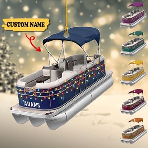 May include: A navy blue pontoon boat Christmas ornament with colourful string lights and a dark blue canopy. The boat has the name "ADAMS" on the side. Additional boat colour options are shown in purple, green, yellow, burgundy, and brown.
