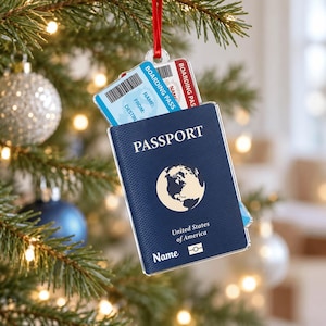 May include: A flat, rectangular Christmas tree ornament shaped like a dark blue passport with a globe icon, the text "PASSPORT", "United States of America", and "Name". A light blue boarding pass with a barcode is tucked inside the top.