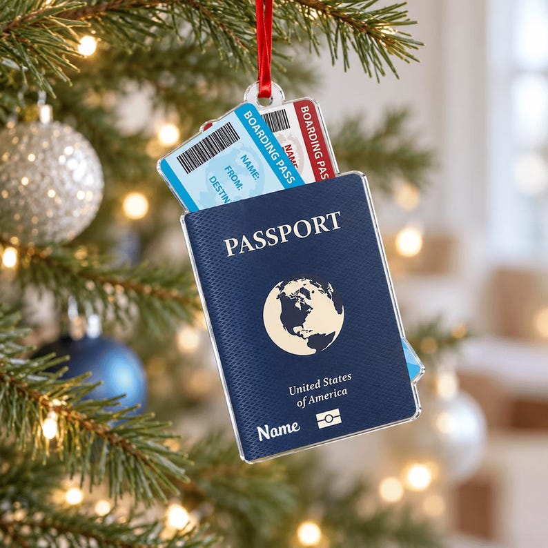 May include: A flat, rectangular Christmas tree ornament shaped like a dark blue passport with a globe icon, the text "PASSPORT", "United States of America", and "Name". A light blue boarding pass with a barcode is tucked inside the top.