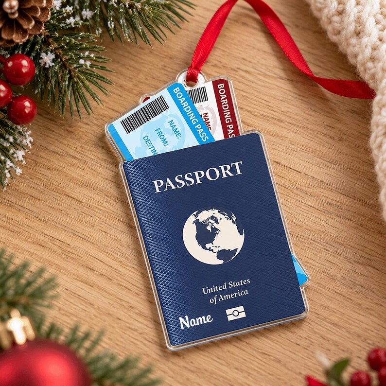 May include: A flat, rectangular Christmas tree ornament shaped like a passport with a dark blue cover, a white globe icon, and the text Passport, United States of America, and Name. A light blue boarding pass is tucked inside the top.