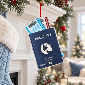 May include: A dark blue passport-shaped Christmas ornament featuring a white globe icon, the text PASSPORT, United States of America, and Name, with a light blue boarding pass tucked inside, all hanging from a red ribbon loop.