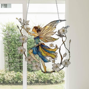 May include: A stained glass fairy with blue wings and a yellow and blue dress, surrounded by white flowers. The fairy is hanging from a silver chain.