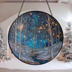 May include: Round stained glass panel depicting a winter forest scene. The artwork features a dark blue and teal background with gold-colored accents, trees, and small lights. The panel is framed in black and hangs from a chain.