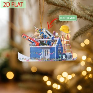 May include: A blue house-shaped Christmas ornament with a ladder, tools, and a yellow hard hat. The ornament has the text "YOUR NAME" and "CUSTOM NAME". The ornament is decorated with string lights and a gold hanging cord.