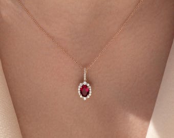 May include: A delicate gold necklace with a red gemstone pendant surrounded by smaller white gemstones.