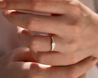 May include: A delicate gold ring with a row of small diamonds and a larger, rectangular diamond in the center.