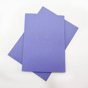 Image shows a purple card with the words happy father's day written in grade 1 UEB braille. A matching purple envelope is beneath the card.