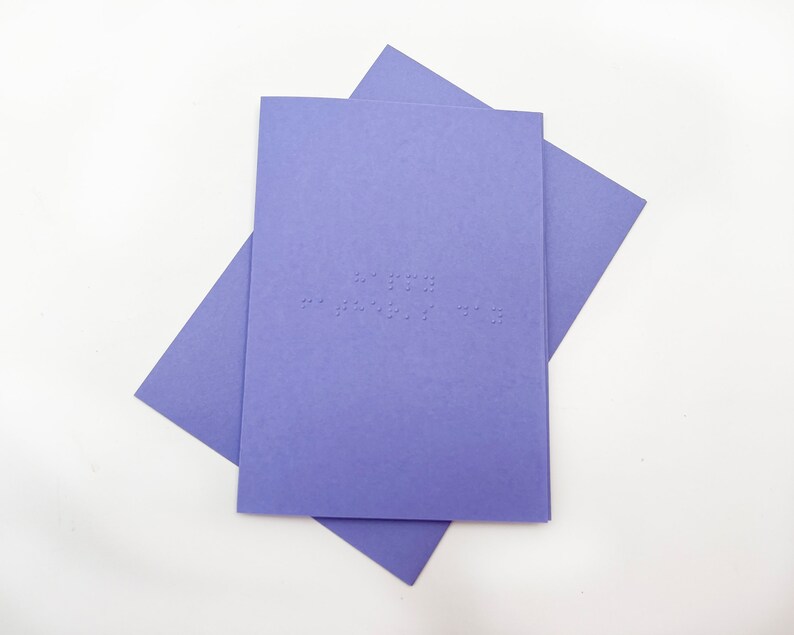 Image shows a purple card with the words happy father's day written in grade 1 UEB braille. A matching purple envelope is beneath the card.