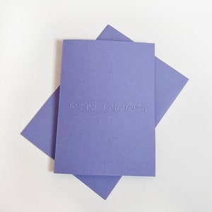 Image shows a purple card with the words happy birthday written in grade 1 UEB braille. A matching purple envelope is beneath the card.