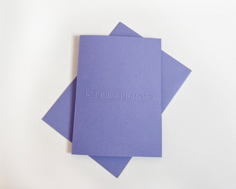 Image shows a purple card with the words happy birthday written in grade 1 UEB braille. A matching purple envelope is beneath the card.
