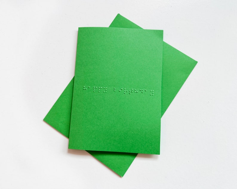 Image shows a green card with the words happy birthday written in grade 1 UEB braille. A matching green envelope is beneath the card.