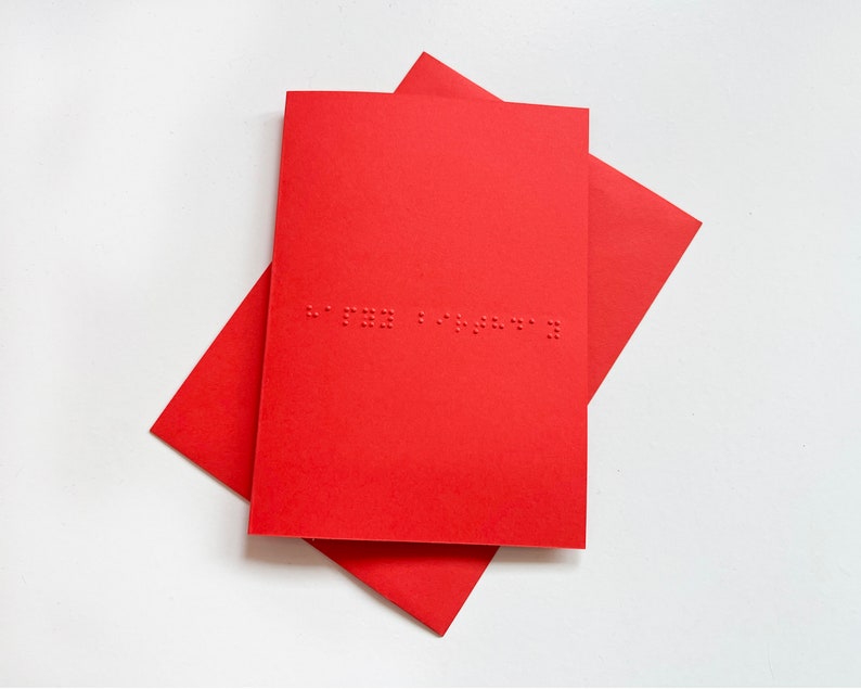 Image shows a blue card with the words happy birthday written in grade 1 UEB braille. A matching red envelope is beneath the card.