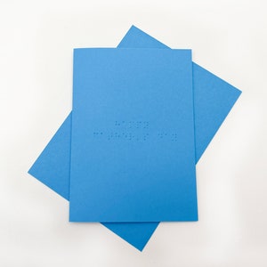 Image shows a blue card with the words happy father's day written in grade 1 UEB braille. A matching blue envelope is beneath the card.