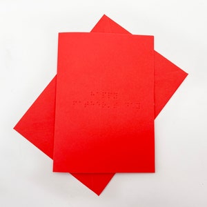 Image shows a red card with the words happy father's day written in grade 1 UEB braille. A matching red envelope is beneath the card.