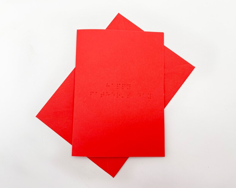 Image shows a red card with the words happy father's day written in grade 1 UEB braille. A matching red envelope is beneath the card.