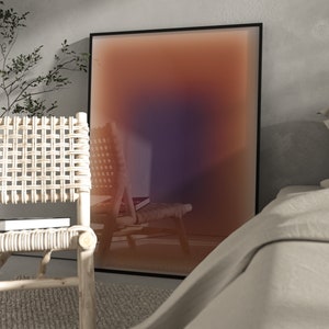 May include: A framed abstract art print with a gradient of orange, pink, and purple colors. The print is hanging on a wall in a room with a wicker chair and a white bed.