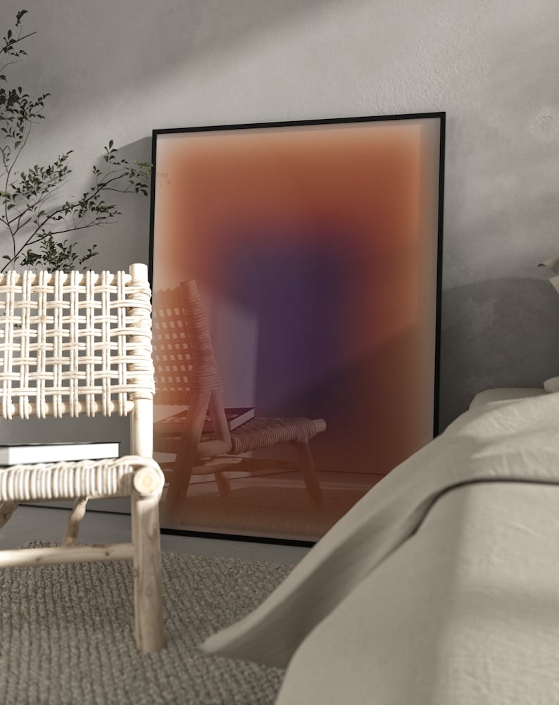 May include: A framed abstract art print with a gradient of orange, pink, and purple colors. The print is hanging on a wall in a room with a wicker chair and a white bed.