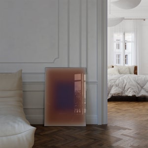 May include: A rectangular abstract art print with a gradient of brown, orange, and purple colors. The print is hanging on a white wall in a room with a white couch and a view of a window.