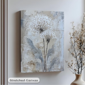a stretched canvas artwork depicting two white flowers with long stems, hanging on a wall next to a vase with dried flowers.