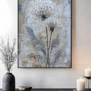 a floating frame-black color painting of a dandelion flower on a wall, with a black shelf below it and a vase with branches and a candle on the shelf.
