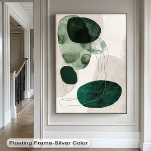 Op de afbeelding: Abstracte kunstprint met overlappende groene en blauwgroene vormen en dunne zwarte lijnen op een neutrale achtergrond. Het kunstwerk is ingelijst in een zilverkleurige zwevende lijst. De tekst "Floating Frame-Silver Color" staat onderaan.