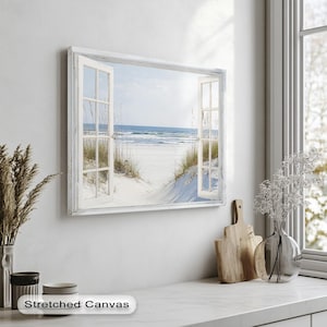 Puede incluir: Una impresión en lienzo estirado que representa una escena de playa vista a través de un marco de ventana blanco. La imagen muestra un camino arenoso que conduce al océano, con agua y cielo azules. La ventana está abierta y el marco tiene un aspecto desgastado.