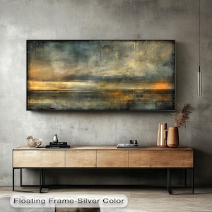 May include: A rectangular abstract landscape painting with a black frame. The artwork features a blend of blues, yellows, and browns, depicting a seascape with a dramatic sky. The painting hangs above a wooden cabinet with black metal legs.