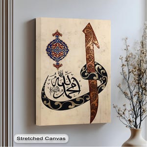Könnte beinhalten: Leinwandkunst mit arabischer Kalligraphie in Schwarz und Gold auf beigem Hintergrund. Das Kunstwerk zeigt ein verziertes Pfeildesign und ein dekoratives Medaillon mit blauen und roten Akzenten. Der Text "Stretched Canvas" steht unten.