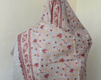 May include: A light gray shawl with intricate floral embroidery in shades of red and orange. The shawl features a detailed border design and a repeating floral pattern across the fabric. The fabric is draped, showcasing the design.