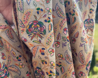 May include: A beige shawl with a floral pattern in shades of pink, red, blue, green, and yellow. The shawl is made of a soft, lightweight fabric and is perfect for adding a touch of elegance to any outfit.