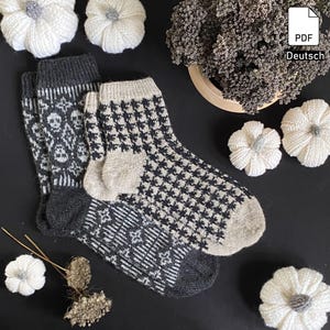 May include: A pair of black and white knitted socks with a skull and crossbones pattern on one sock and a houndstooth pattern on the other sock. The socks are on a black background with white flowers.