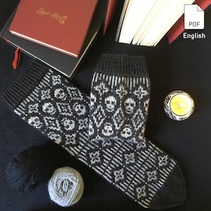Könnte beinhalten: Ein Paar schwarze und weiße Stricksocken mit Totenkopf-Muster. Die Socken liegen auf einer schwarzen Oberfläche mit einer Kerze und Wollknäuel.