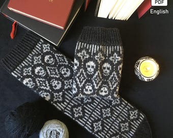 May include: A pair of black and white knit socks with a skull pattern. The socks are lying on a black surface with a candle and yarn balls.