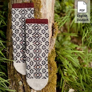 Könnte beinhalten: Ein Paar Strickstrümpfe mit cremefarbener Basis und einem sich wiederholenden geometrischen Rautenmuster in Schwarz und Dunkelrot. Die Socken haben ein einfarbiges, dunkelrotes Rippbündchen am oberen Rand und eine schlichte, cremefarbene Zehenpartie.