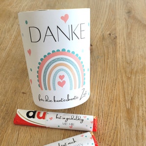 May include: Three chocolate bars wrapped in red foil with white paper labels. The labels have pink hearts and text in German. The text on the labels reads "Du bist so geduldig mit mir", "Du lässt mich neues entdecken", and "Du bringst mir ein Lächeln ins Gesicht".