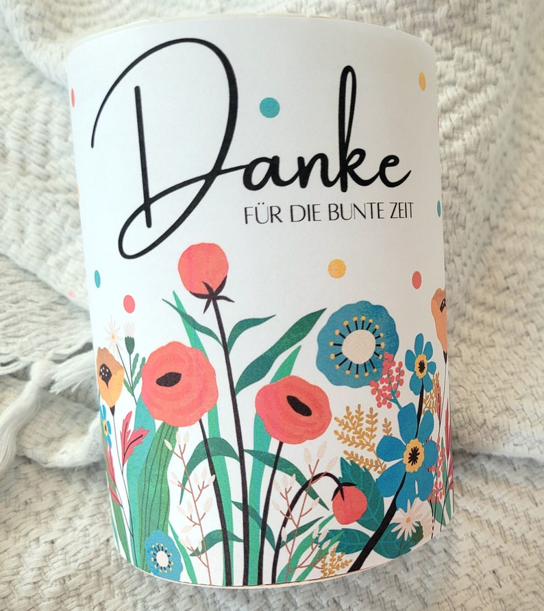 May include: White cylindrical container with a floral design and the text "Danke f&uuml;r die bunte Zeit". The flowers are red, blue, yellow, and green.