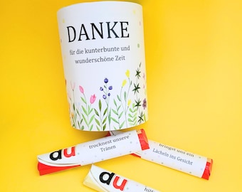 May include: A white cylindrical container with the word "DANKE" and floral illustrations. Below the container are three wrapped candies with German text. The background is a solid yellow.