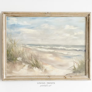 May include: A framed painting of a beach scene with blue sky, white clouds, and a sandy beach with green grass in the foreground. The ocean is in the background with waves crashing on the shore. The frame is a light wood color.