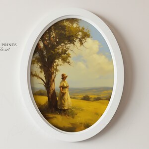 May include: A framed painting of a woman standing in a field with a tree and a distant view of rolling hills. The sky is blue with white clouds. The painting is in a white oval frame.