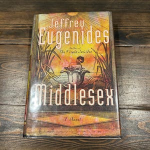 May include: A hardcover book titled "Middlesex" by Jeffrey Eugenides. The cover features a colorful illustration of a person in a flower, with text in a stylized font. The book is a novel.